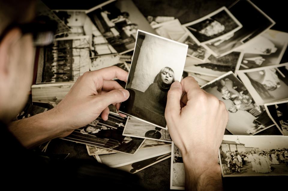 Zwei Hände halten ein altes Schwarz-Weiß-Foto über einem Stapel weiterer Fotos