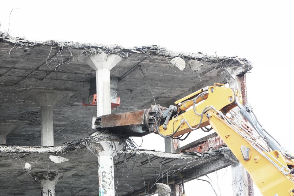 Gelber Abrissbagger bricht die Decken eines Betongebäudes ab