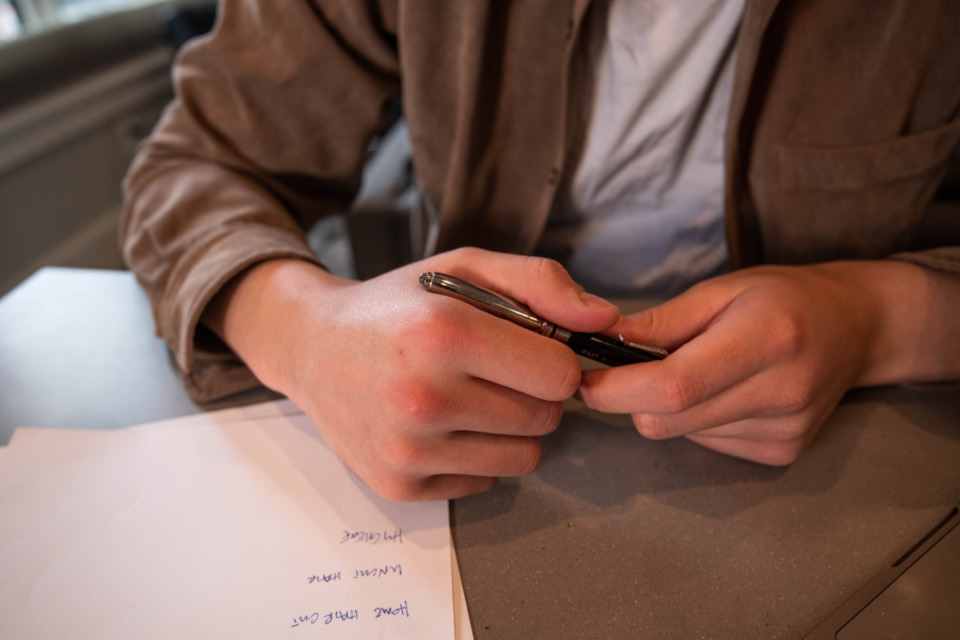 Person sitzt mit einem Stift in der Hand vor einem beschriebenen Blatt Papier